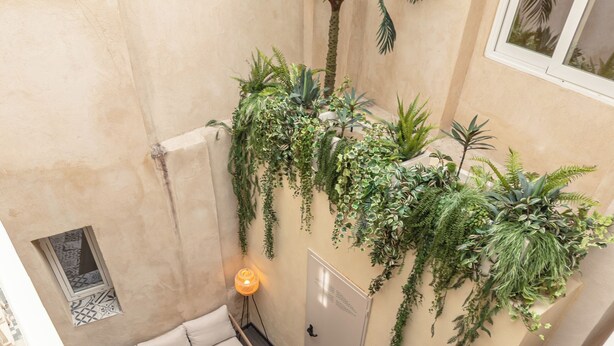 Un balcone interno con un divano, due poltrone, un tavolino e una parete decorata con piante.