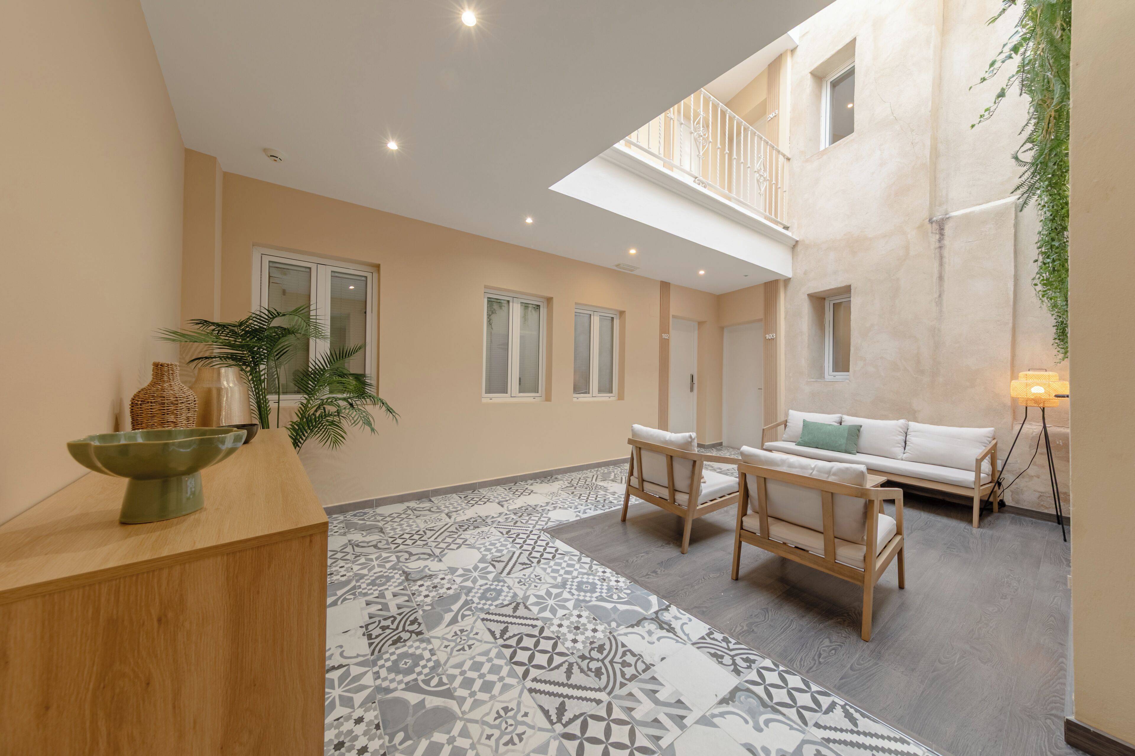 A spacious indoor area with a wooden reception desk, a patterned floor, a white sofa, and a balcony with a railing.