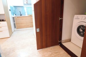 Ein Waschraum mit einer Waschmaschine, einer Holztür und einem Küchenbereich im Hintergrund.