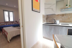 Ein Schlafzimmer mit einem Bett, einem Fenster und einer Tür zu einer Küche mit Spüle und Arbeitsplatte.