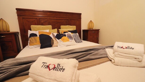 A neatly made bed with a grey blanket, multiple pillows, and two folded towels with 'Travellito' embroidered on them. - Beautiful private villa for 4 people with A/C, WIFI, TV and panoramic view (Otranto)