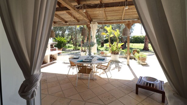 Eine Terrasse im Freien mit Tisch und Stühlen, umgeben von Blumentöpfen und einer Holzw pergola.