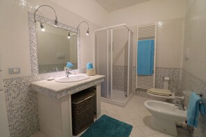 Een badkamer met een wastafel, spiegel, douche, toilet en bidet.