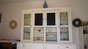 Ein weißer Schrank mit Glastüren, beschriftet mit 'Martha's Vineyard Recipes', der verschiedene Gerichte und Küchenutensilien beherbergt.