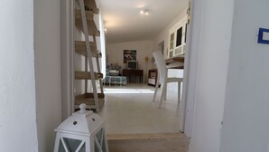Ein Flur mit einer weißen Laterne, Holzstühlen und einer Treppe zu einem Zimmer mit Bett und Schreibtisch.