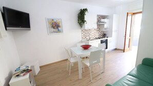 Una cucina moderna con mobili bianchi, zoccolo piastrellato e piano cottura integrato. C'è una zona pranzo con tavolo e sedie bianche e un divano verde in primo piano.
