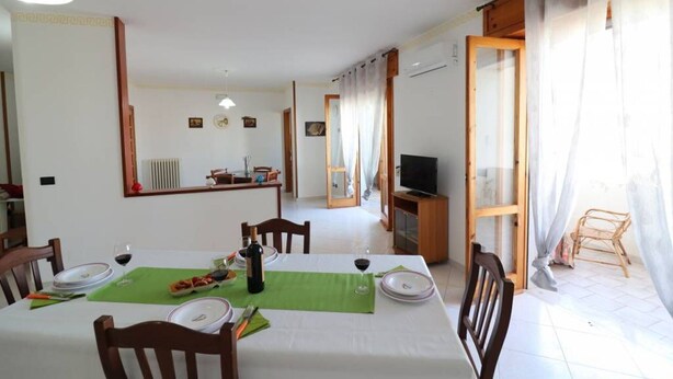 A dining area with a table set for two, a television on a stand, and a view of the outside through a door. - Wonderful  villa for 8 guests with A/C, WIFI, TV and balcony (Otranto)