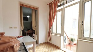 Un pequeño comedor con una mesa y sillas, una ventana con cortinas y vistas al balcón exterior.