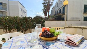 Et bord dækket udendørs med en skål frugt, glas og en avis.