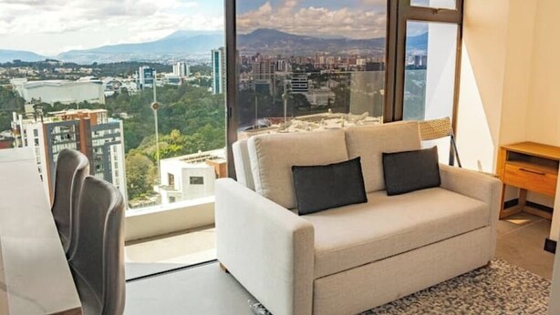 A modern living room with a large window offering a cityscape view. - *Comfortable apartment* minutes away from cayala (Ciudad de Guatemala)