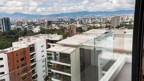 A high-rise building with multiple floors, large windows, and a view of a cityscape with various buildings and mountains in the distance. - *Comfortable apartment* minutes away from cayala (Ciudad de Guatemala)