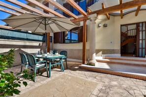 Une terrasse extérieure avec une table et des chaises, un grand parasol et un escalier menant à un niveau supérieur.