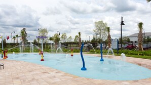 Ein Wasser-Spielbereich im Freien mit mehreren Wasserstrahlen und einem gefliesten Boden.