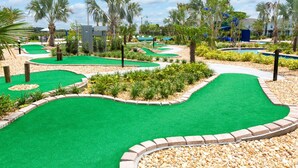 Ein Minigolfplatz mit mehreren grünen Spielbahnen, umgeben von angelegten Gärten und Palmen.