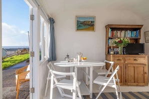 Une pièce avec une table et des chaises blanches, une bibliothèque en bois, un tableau et une vue sur la mer.