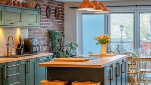 Une cuisine moderne avec un îlot central, des meubles de couleur verte et des tabourets en bois.