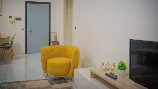 Un salon moderne avec un fauteuil jaune, un téléviseur à écran plat, une petite plante et une télécommande posée sur une console en bois.