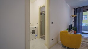 Un salon moderne avec un fauteuil jaune, un lave-linge et une plante en pot.