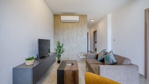 Ein modernes Wohnzimmer mit Flachbildfernseher, Sofa, Couchtisch und einer Pflanze.