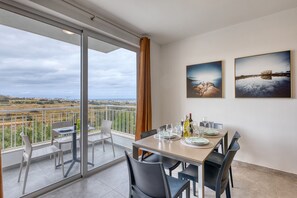 A dining area with a table set for four, a balcony with a view, and two framed pictures on the wall. - Modern 2 bedroom apartment, Valley Views KARP1-4 (San Gwann)