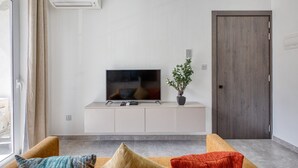 En moderne stue med et fladskærms-tv på et hvidt tv-møbel, en potteplante og en trædør.