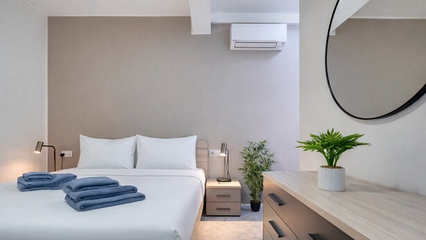 Et moderne hotelværelse med seng, sengeborde, en stueplante, et kommode og en aircondition.