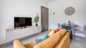 En moderne stue med et fladskærms-tv, en sofa, et spisebord med stole og et ur på væggen.