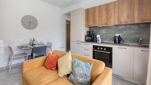 Et moderne køkken med træskabe, et spiseområde med bord og stole, samt en opholdsstue med sofa.