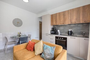 A modern kitchen with wooden cabinets, a dining area with a table and chairs, and a living room with a sofa. - Charming 2 bedroom Apartment, Valley Views KARP1-5 (San Gwann)