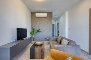A modern living room with a flat-screen TV, a wooden coffee table, a grey sofa, and a potted plant. - Central and modern Apartment, Valley Views KARP1-6 (San Gwann)