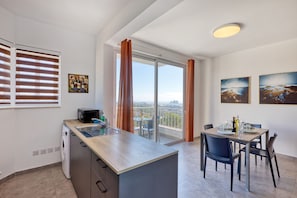 A modern kitchen with a built-in oven, a microwave, and a sink. There is a dining area with a table and chairs, and a balcony with a view of the city. - Central and modern Apartment, Valley Views KARP1-6 (San Gwann)