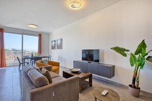 A modern living room with a sofa, coffee table, TV, and a balcony with a view. - Central and modern Apartment, Valley Views KARP1-6 (San Gwann)
