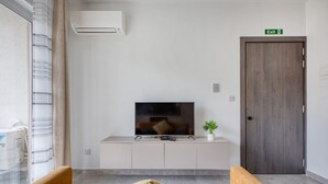 Un soggiorno moderno con una televisione a schermo piatto, un divano, una piccola pianta e una porta in legno con la scritta 'Exit'.