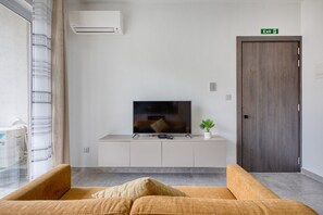 Ein modernes Wohnzimmer mit Flachbildfernseher, einer Couch, einer kleinen Pflanze und einer Holztür mit der Aufschrift 'Exit'.