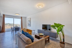 A modern living room with a sofa, coffee table, TV, and a large plant. - 2 bedroom flat with balcony, valley views KARP1-8 (San Gwann)