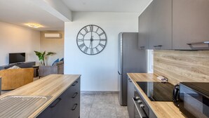A modern kitchen with a large wall clock, built-in appliances, and a wooden countertop.