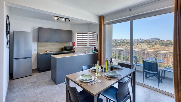 A modern kitchen with a central island, a dining area with a table set for two, and a balcony with a view of the city.