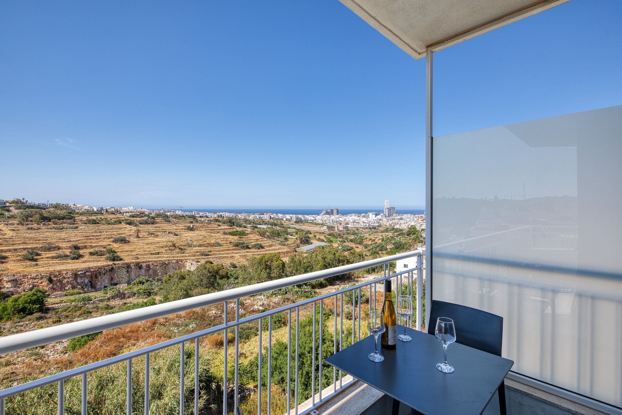 A balcony with a table, two wine glasses, and a bottle.