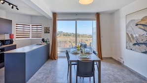 A modern kitchen with a dining area, a large window with curtains, and a view of the landscape.