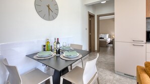 Ein moderner Essbereich mit einer runden Wanduhr, einem für vier Personen gedeckten Tisch und einer Küche im Hintergrund.