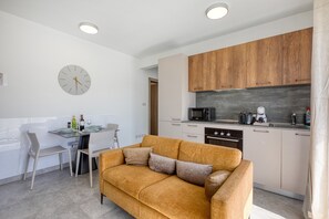 A modern kitchen with wooden cabinets, a dining area with a table and chairs, and a sofa. - Refined 2 bedroom apartment with balcony KARP1-9 (San Gwann)