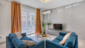 Un soggiorno moderno con due divani blu, un tavolino da caffè, una pianta in vaso e una TV a schermo piatto montata a parete.