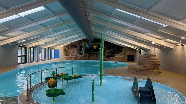 An indoor pool with water slides and a rock formation backdrop.