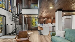 Ein modernes Interieur mit Wendeltreppe, einem grünen Sofa, einer Küchenzeile und einem Essbereich.