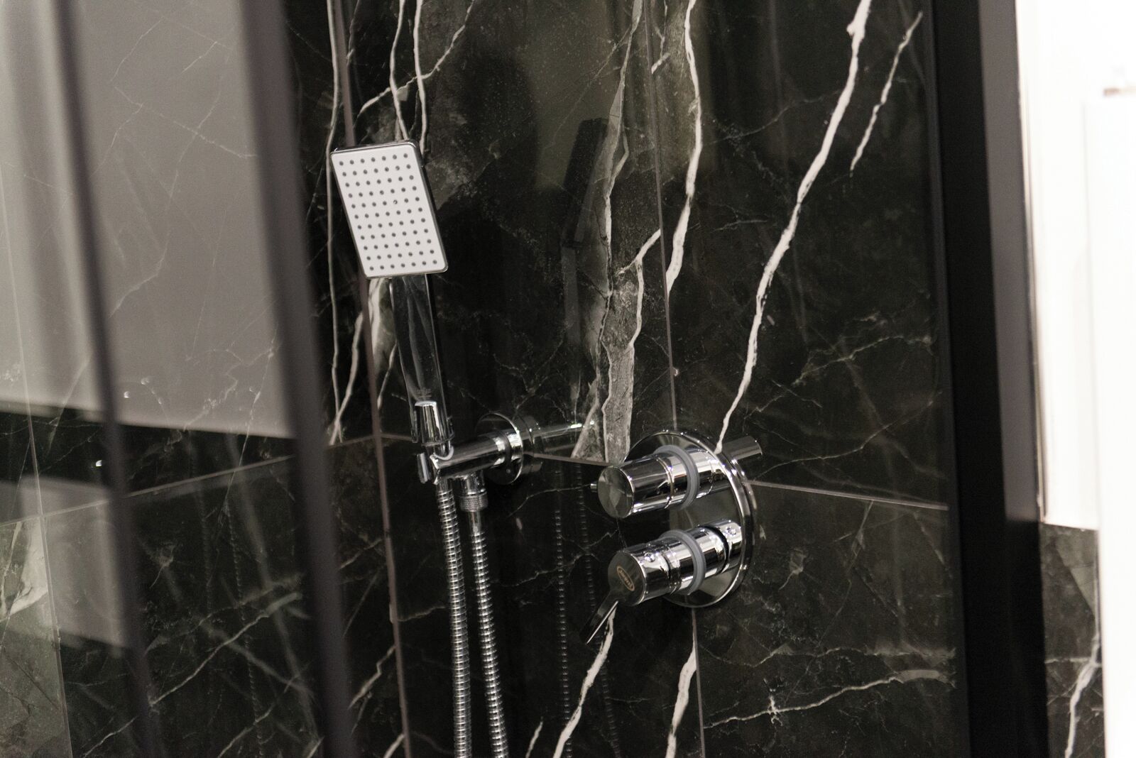 Une douche équipée d’un pommeau de douche à main et d’un robinet mural, le tout installé sur un mur en marbre.