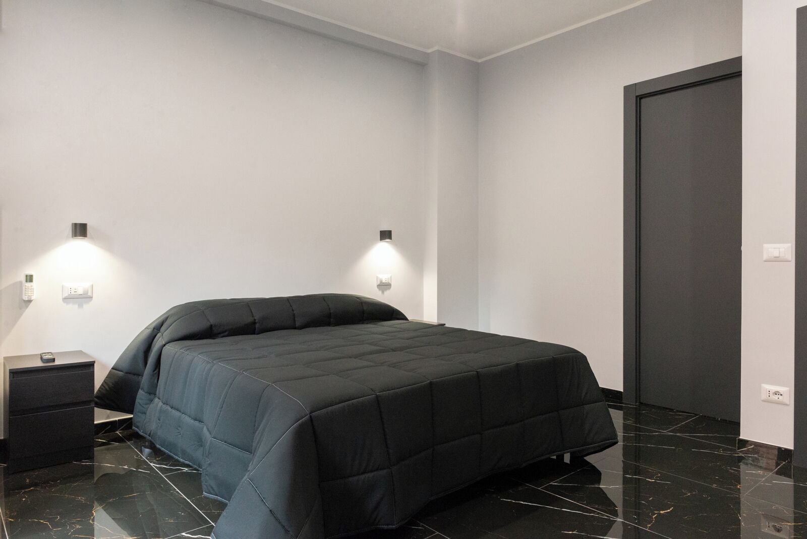 A modern bedroom with a large bed, two bedside tables, and a dark door.