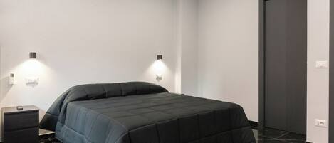 Un dormitorio moderno con una cama grande, dos mesitas de noche y una puerta oscura.