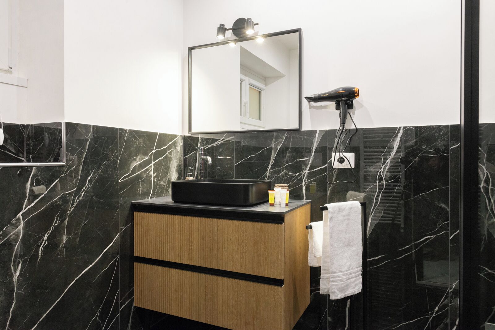 Een moderne badkamer met een zwart marmeren wastafel, een grote spiegel en een haardroger bevestigd aan de muur.