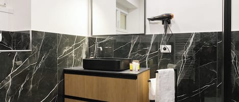 A modern bathroom with a black marble vanity, a large mirror, and a hairdryer mounted on the wall.