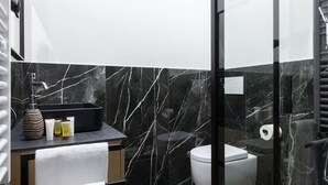 Une salle de bain moderne avec un pare-baignoire en marbre noir, une douche en verre et des toilettes blanches.